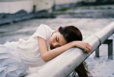 a woman leaning on a metal rail with her head resting on her hand and eyes closed