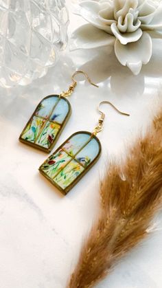 a pair of earrings sitting on top of a table next to a white flower and feather