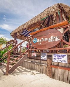 a sign that says my paradise beach club on the side of a wooden building with stairs leading up to it