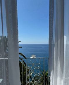 an open balcony overlooking the ocean with white drapes and coffee cup sitting on it