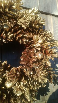 a wreath made out of gold leaves and pine cones on top of a wooden table