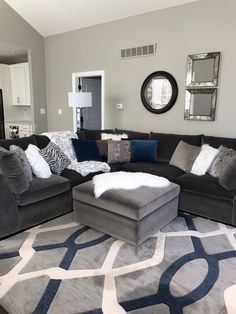 a living room with gray couches and blue pillows on the rug in front of it