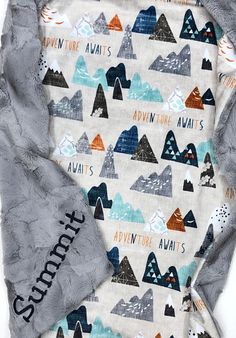 a blanket with mountains on it and the words adventure printed on it, sitting next to a pillow