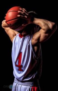 a man holding a basketball over his head with both hands and looking down at it