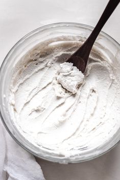 a wooden spoon in a glass bowl filled with whipped cream on top of a white cloth