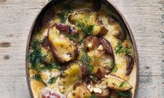 a dish filled with potatoes and herbs on top of a wooden table