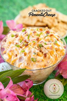 a bowl filled with cheese and bacon on top of a green surface next to pink flowers