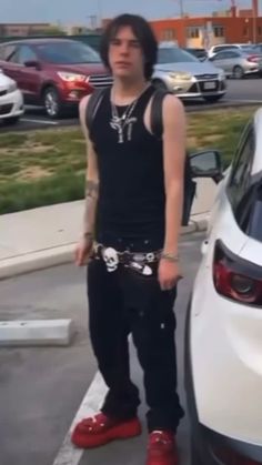 a man standing next to a white car in a parking lot with red shoes on