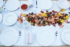 the table is set with white plates, silverware, and corn on the cob