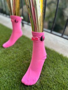 two pink socks with flowers in them sitting on the grass next to a metal fence