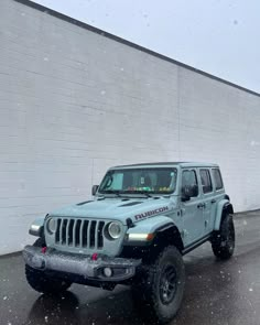 a blue jeep parked in front of a white brick building on a snowy day with snow falling