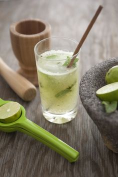 a glass filled with green liquid next to some limes and other ingredients on a wooden table