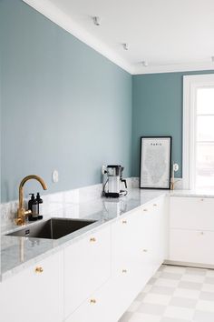 a kitchen with blue walls and white cabinets, gold pulls on the faucet