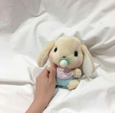 a person is holding a small stuffed animal in their hand on a white bed sheet