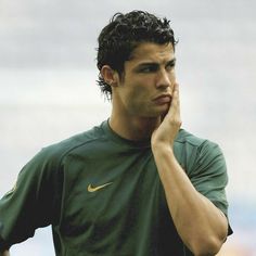 a young man in a green shirt holding his hand to his face while standing on a soccer field