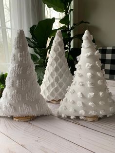 three white christmas trees sitting on top of a wooden table