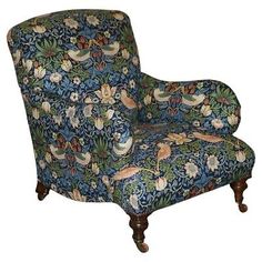 a blue floral chair sitting in front of a wooden paneled wall with birds and flowers on it