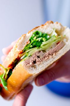 a hand holding a sandwich with meat, lettuce and tomato