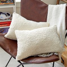 two white pillows sitting on top of a brown leather chair next to a book shelf