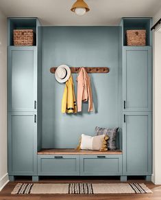 an entryway with blue painted cabinets and coat racks on the wall next to a white rug