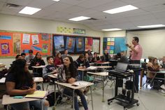 a classroom full of students sitting at desks and one man standing in front of them