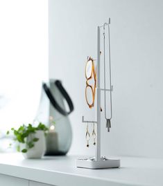 a pair of glasses is hanging from a stand on a white shelf next to a potted plant