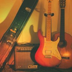 guitars and amps sit on the floor in front of a wall with a guitar case