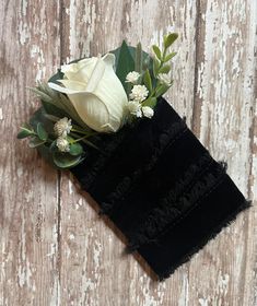 a white rose and some green leaves on a black piece of cloth with wood background