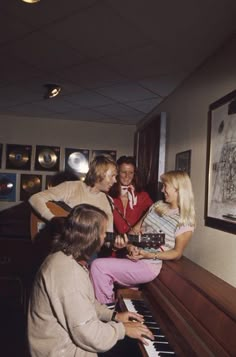 a group of people standing around a piano in a room with pictures on the wall