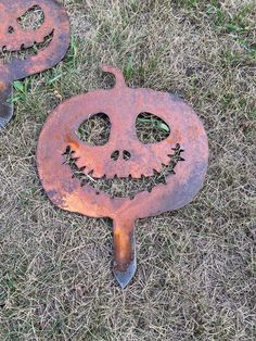 two rusty metal jack - o'- lantern faces on the ground with grass around them