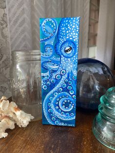 an octopus painting on a wooden table next to jars and glass containers with seashells