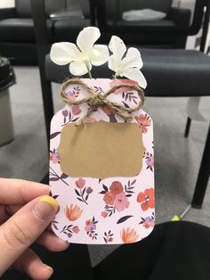 a person holding up a small tag with flowers on it in front of a chair