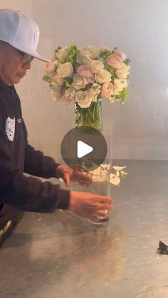 a man in a white hat is arranging flowers on a table with a vase and scissors