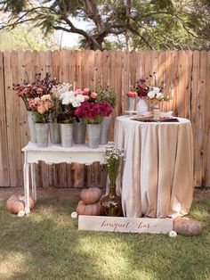 an outdoor table with flowers and vases sitting on it's side in front of a wooden fence