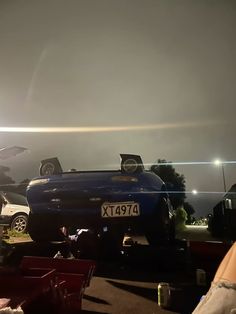 the back end of a blue car parked on top of a parking lot at night