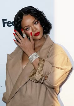 a woman with black hair and red nail polish holding her hand up to her face