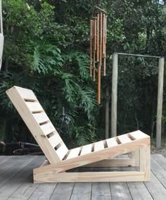 a wooden lounge chair sitting on top of a wooden deck next to a green forest