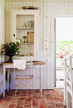 a kitchen with white walls and red tile flooring on the floor, along with an old china cabinet