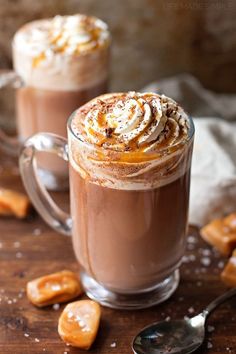 two glasses of hot chocolate with whipped cream and caramel toppings on a wooden table