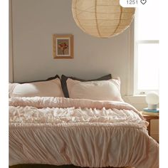 a bed with white sheets and pillows next to a large round light fixture on the wall