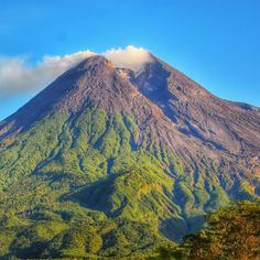 a large mountain covered in green vegetation under a blue sky with white clouds above it