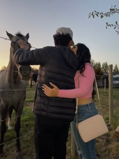 a man and woman standing next to a horse in a fenced in area at sunset