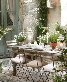 an outdoor dining table with chairs and flowers on the table in front of a stone building