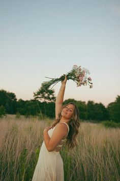 a woman in a white dress holding flowers up to the sky with her arms outstretched