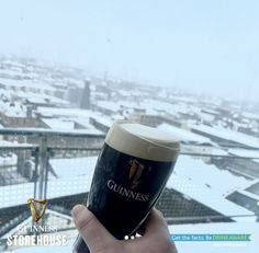 a person holding up a guinness glass in front of a snowy cityscape with the guinness storehouse logo on it