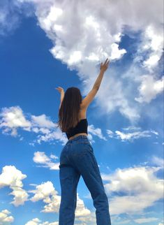 a woman standing on top of a grass covered field under a blue sky with clouds