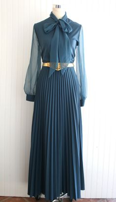 "Circa 1970s, this is a teal dress with perma peleat skirt and sheer sleeves and bow at the neckline.   We have paired it with a gold blet that is not original and is not included.  This dress is without holes or stains.  It is missing it's original belt or sash.  Marked size 14 Estimated size 12 38\" bust 30\" waist full hip 57\" nape to hem  Purveyor's Note: We have searched far and wide, wrestled bears, braved the cold, traversed mountain ranges, fought pirates, swam with sharks and eaten at many a questionable road side taco stand to provide our customers with one of a kind vintage pieces.  Know that whichever piece you choose to make your own has its own story and has traveled through time to get to you.  Though we strive to provide the absolute best, \"pristine\" vintage pieces are r Vintage Teal Dress, Chic Vintage Evening Dress For Fall, Vintage Pleated Dress For Party, Pleated Vintage Dress For Party, Chic Fall Dresses For Vintage Fashion, Retro Dresses For Vintage Events In Fall, Retro Fall Dresses For Vintage Events, Elegant Vintage Fashion Dresses For Fall, Vintage Spring Dresses For Dinner