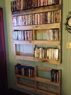 a wooden shelf filled with dvd's on top of a wall next to a clock