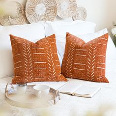 two orange pillows sitting on top of a bed next to a cup and saucer