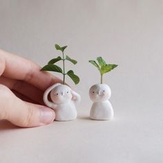 two small white figurines holding plants in their hands